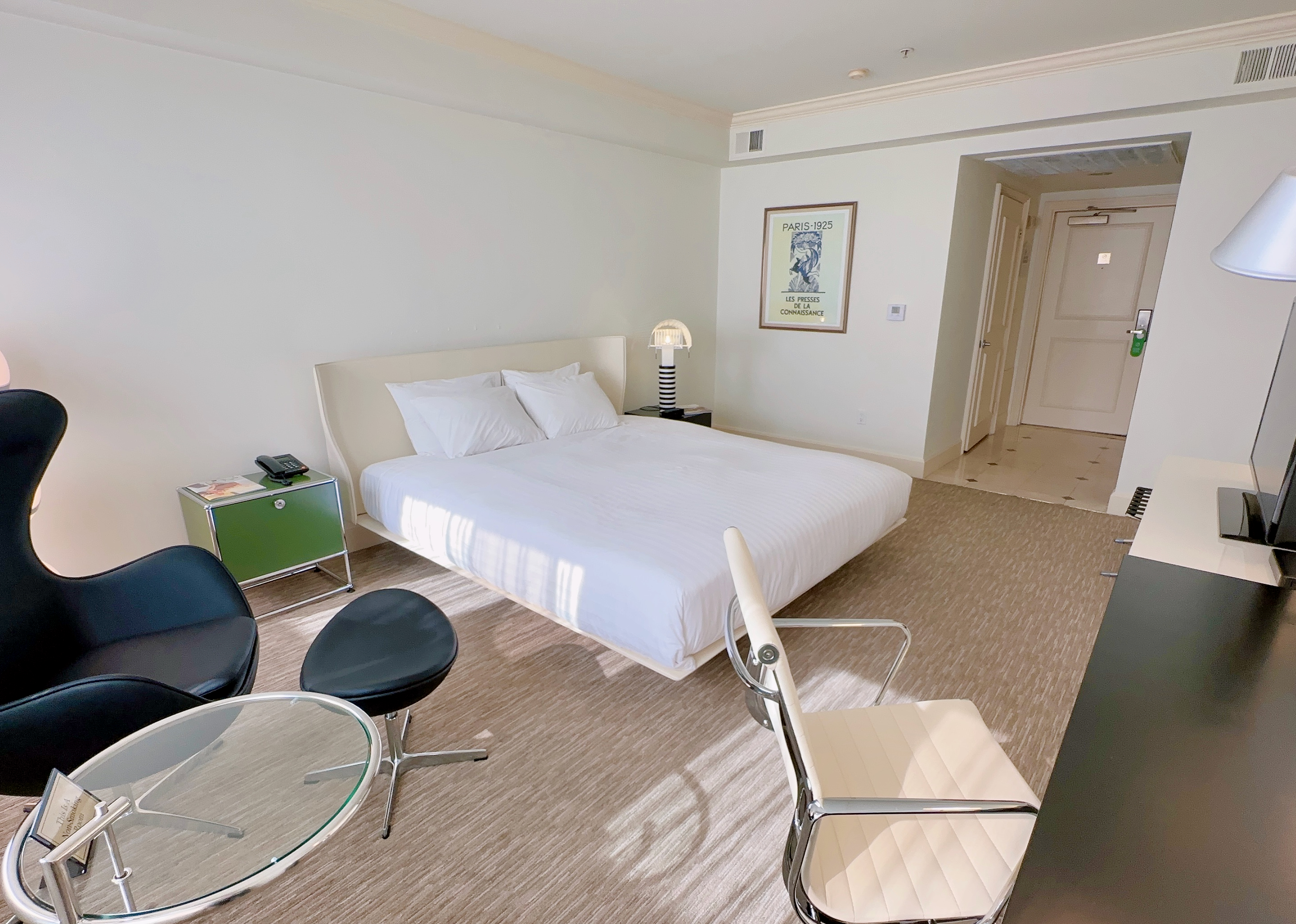 A hotel room with a bed, desk, chairs, and a doorway